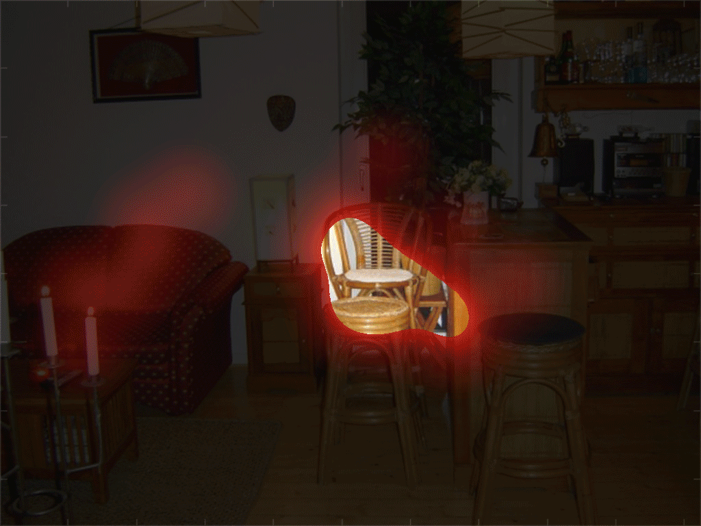 Animated fixation density map showing where subjects tend to look in a scene over the course of a 30 second trial. The fixation density is cumulative. High fixation density is indicated by fully transparent regions of the density map, showing the scene image underneath. The scene that is visible under the density map shows an indoor lounge area that has a red couch as well as a bar with adjacent stools and chairs of wicker construction. The regions most fixated include the coffe table in front of the couch, the seats of chairs in the center of the screen, and objects sitting on the bar counter.